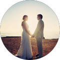 bride and groom facing each other with hands clasped in front of a sunset