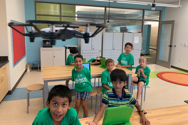 group of campers with tablets looking at a flying drone