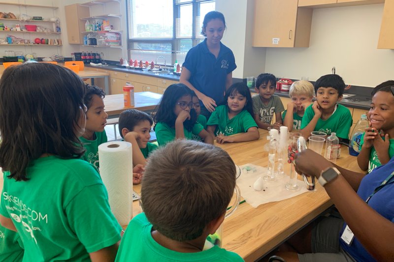 group of young campers sitting around a table watching a science experiment