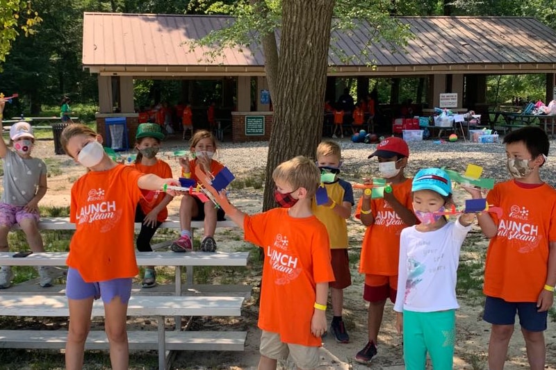 group of campers wearing face masks and orange camp t-shirts playing outside