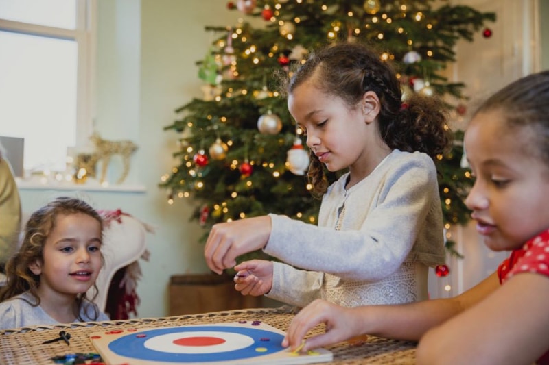 three young girls playing a game in front of a Christmas tree