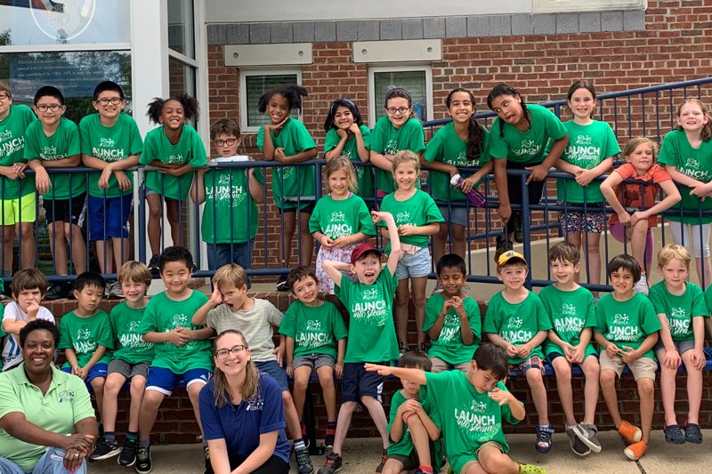 large group of campers in green camp t-shirts posing for a picture