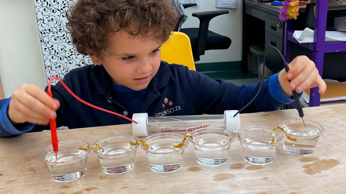 young boy working on electrical experiment with cups of water