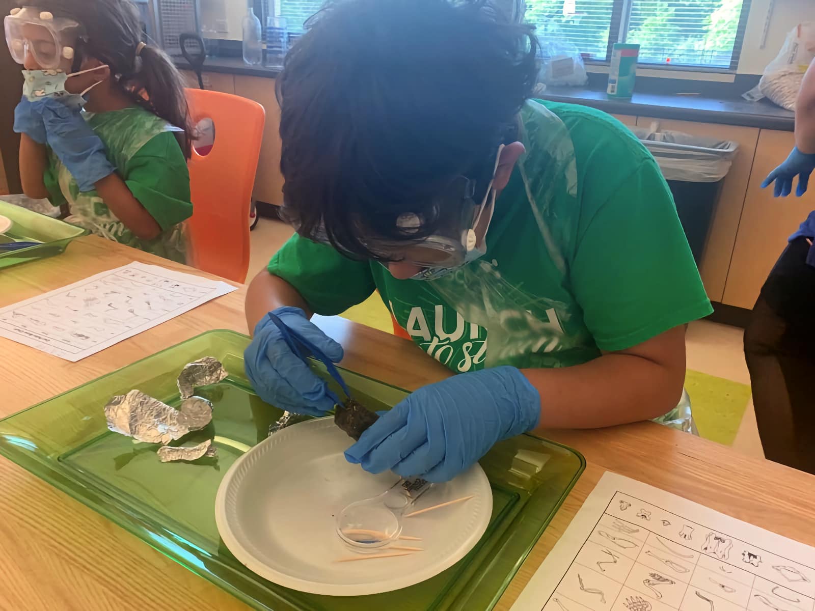 boy wearing gloves and safety goggles using tweezers to dissect something