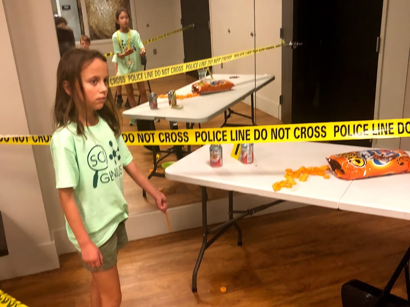 girl looking over a staged crime scene with police tape and an open bag of cheetos