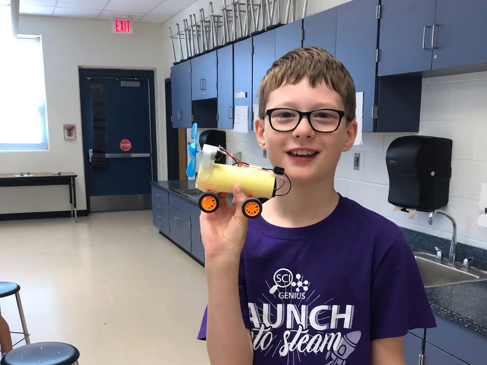boy holding up a model car with a fan connected with wires