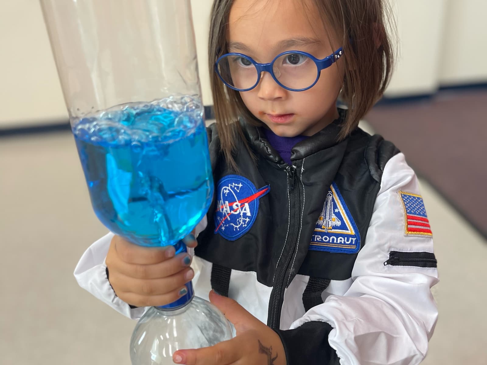 little girl in NASA coat holding tornado experiment