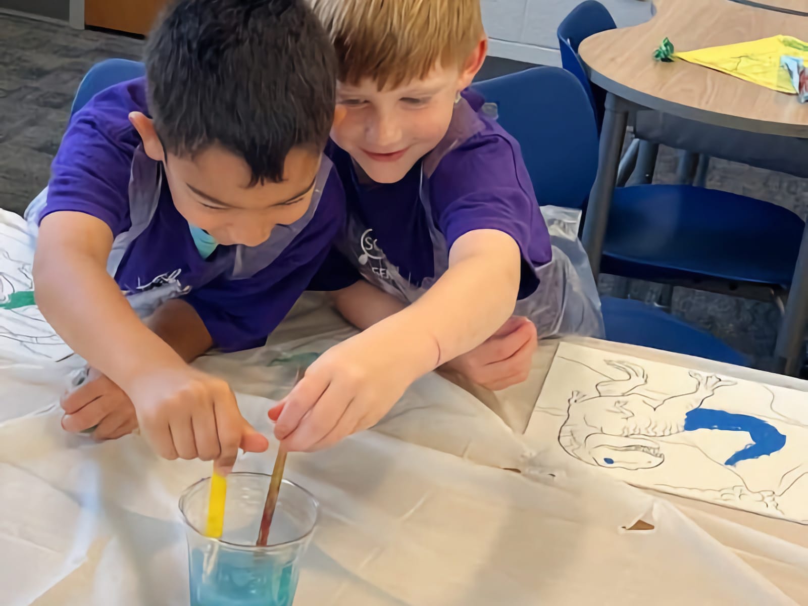 two young boys putting paint brushes into a cup with water