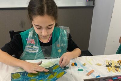 A young girl scout drawing on paper with chalk.