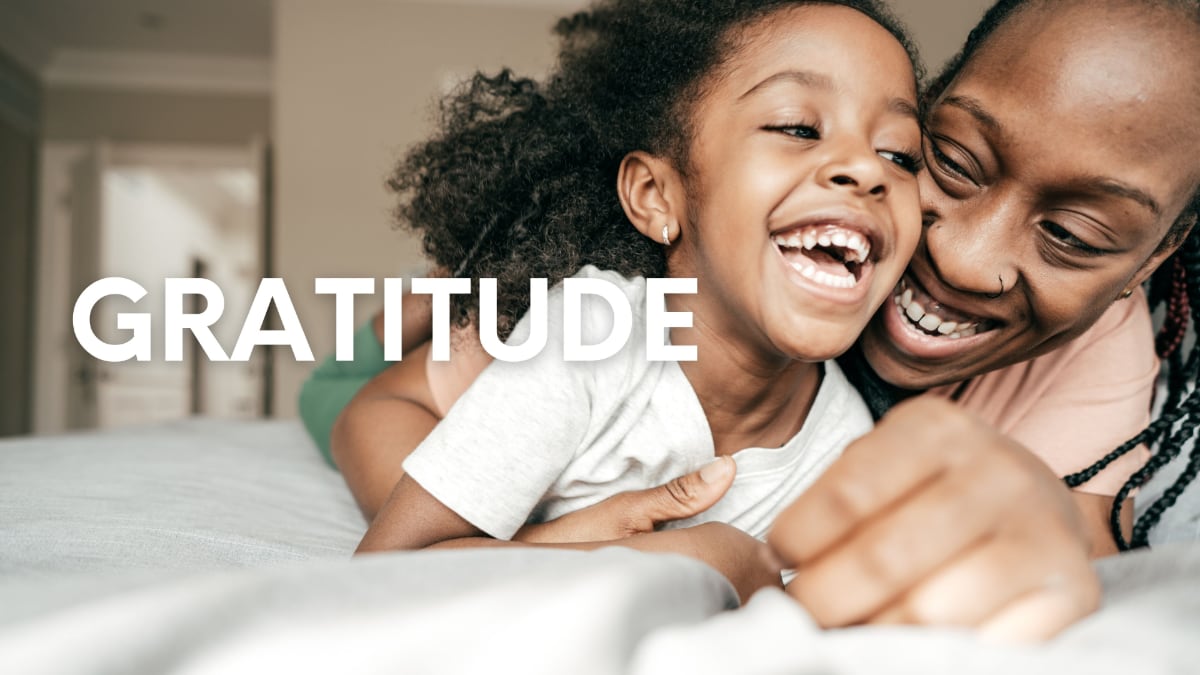 girl and parent cuddling in bed with Gratitude written on top of image