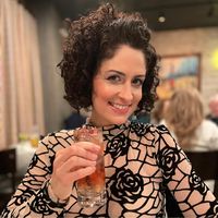 smiling woman with curly hair holding glass up to camera