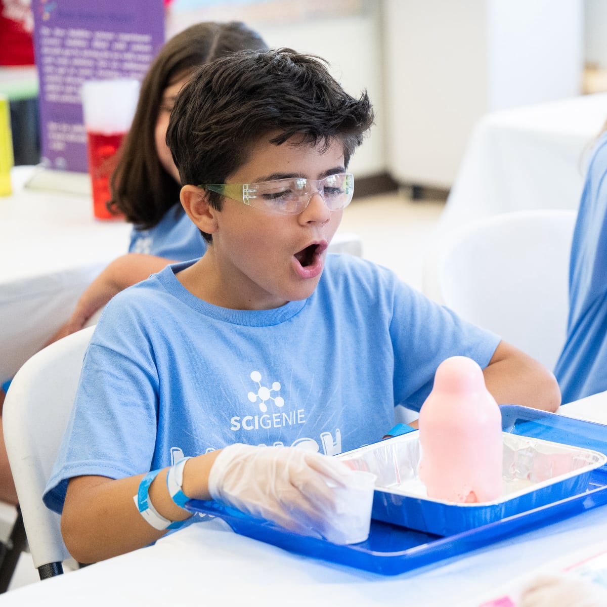 boy wearing safety goggles looking at science experiment in awe