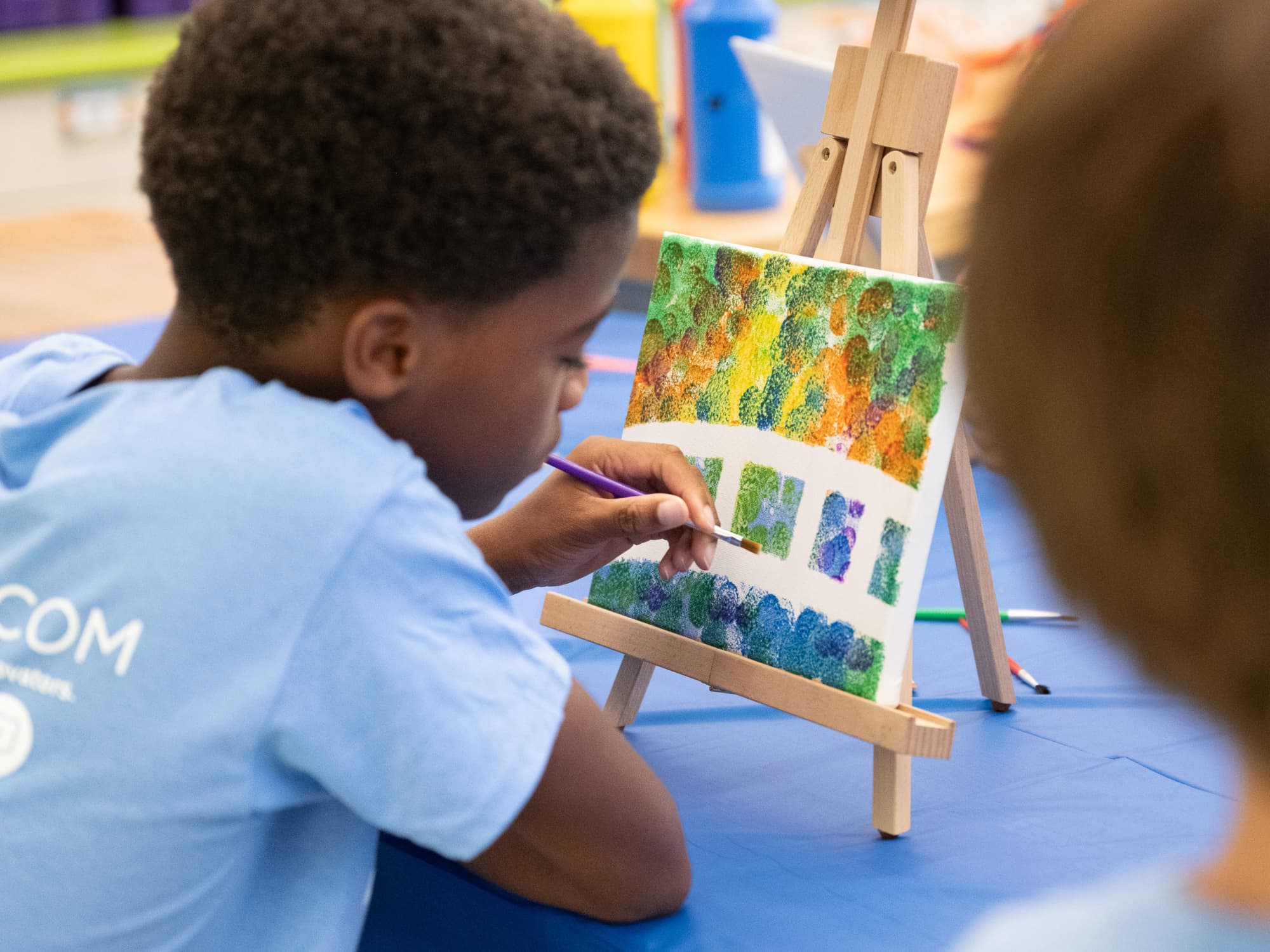 boy holding paintbrush to canvas sitting on an easel