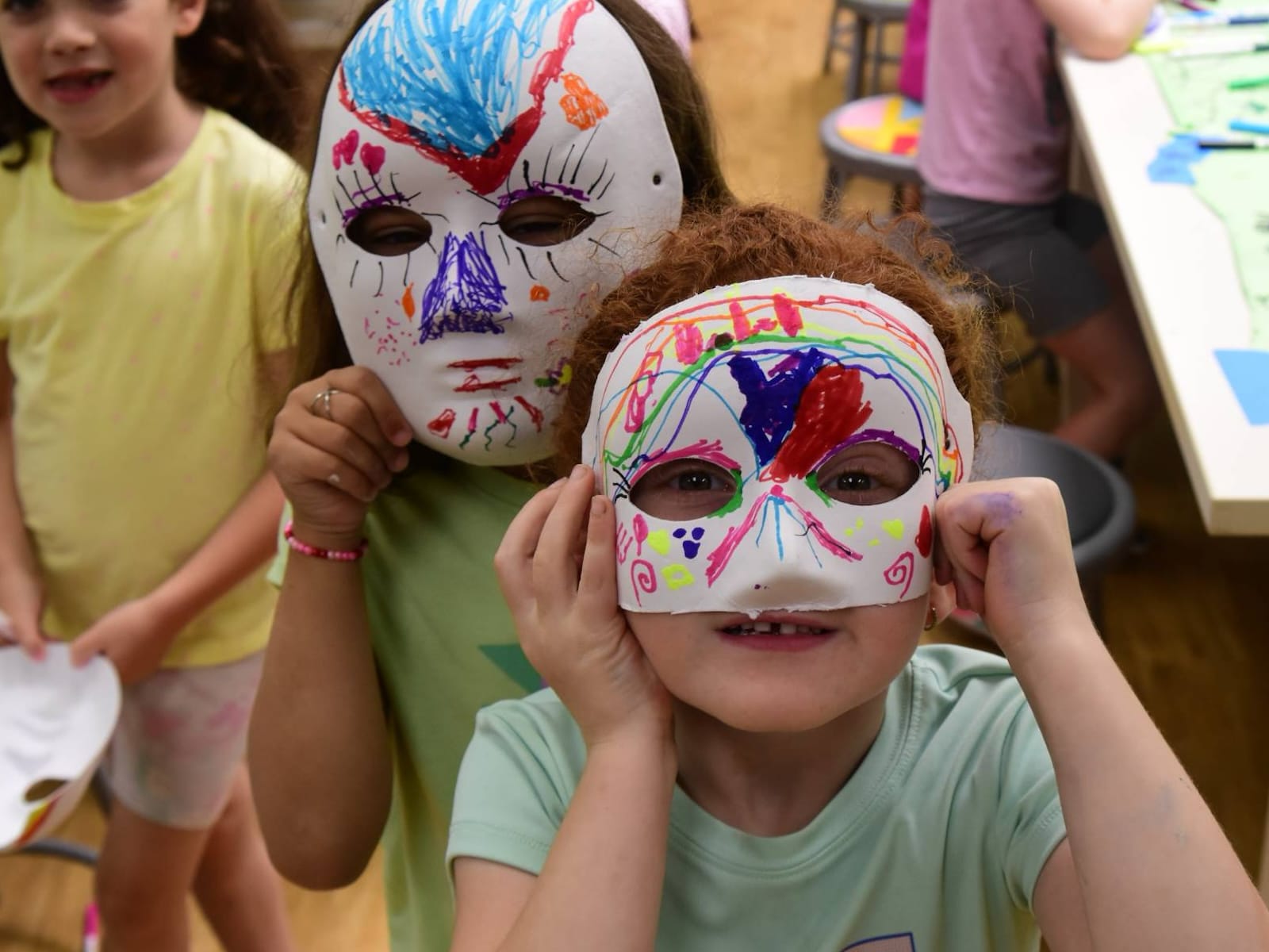 young campers holding up colorfully painted masks they created