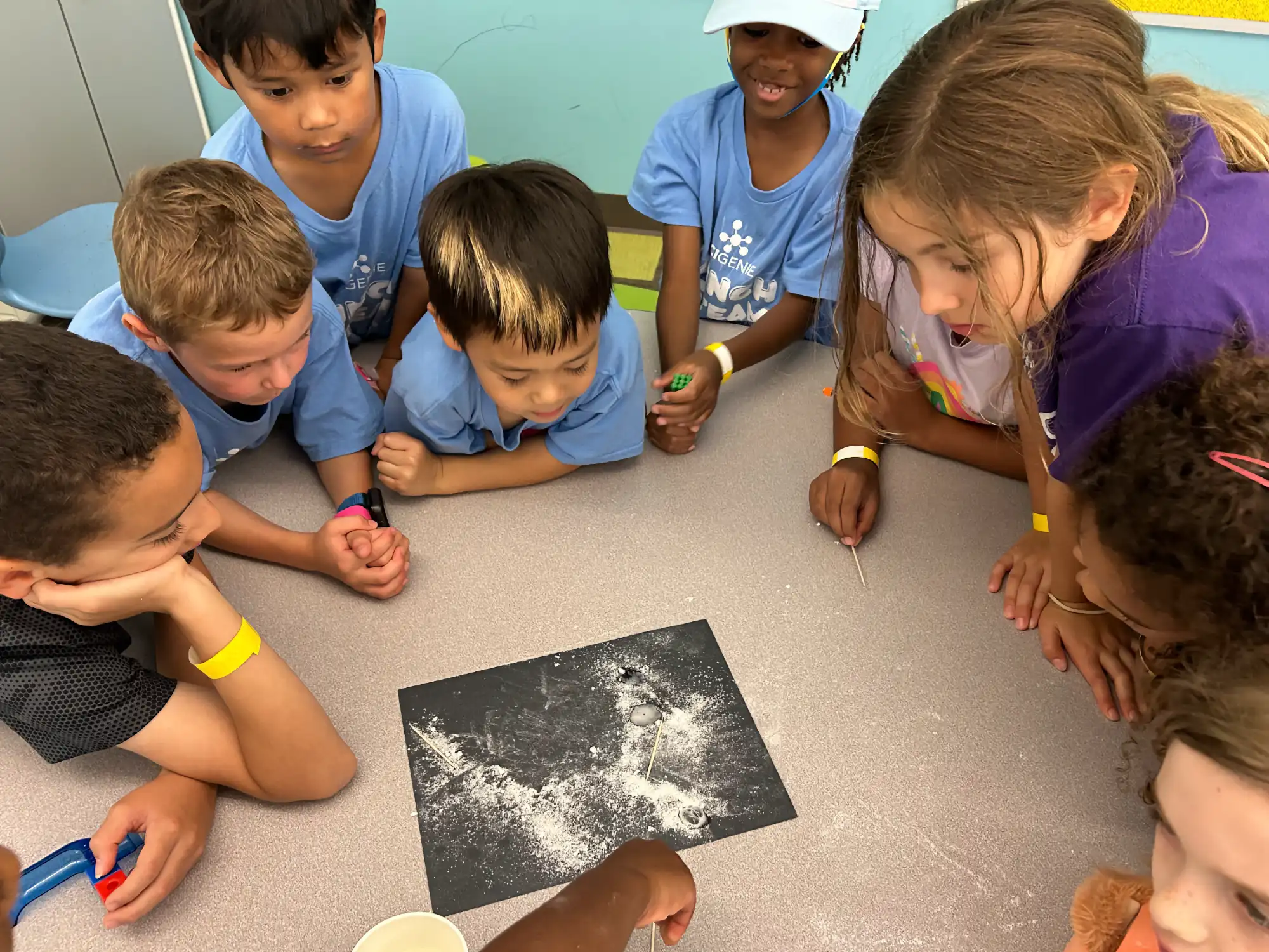 A group of campers looking at powder on a piece of black construction paper.