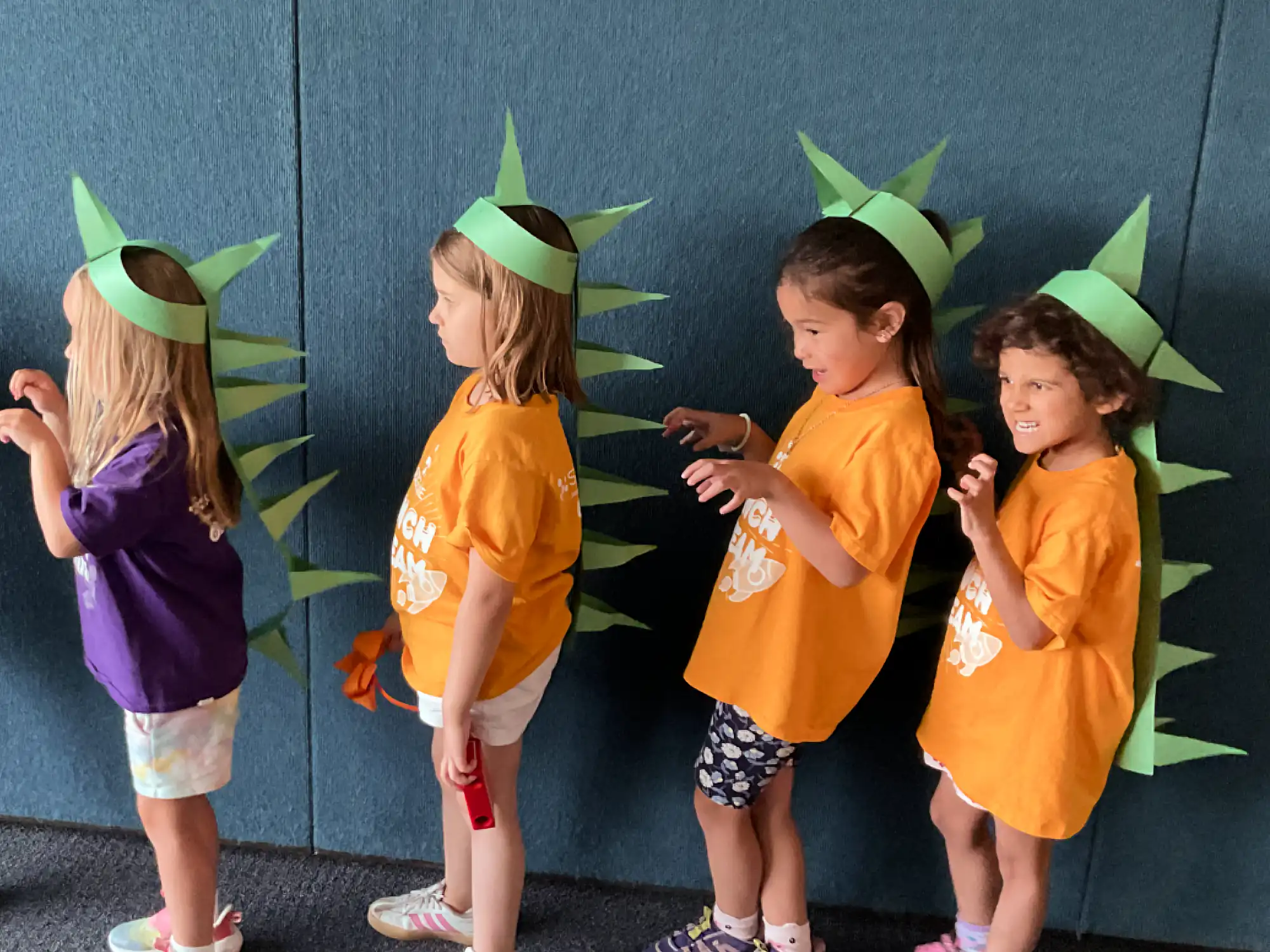 Four young campers wearing dinosaur construction paper spikes.