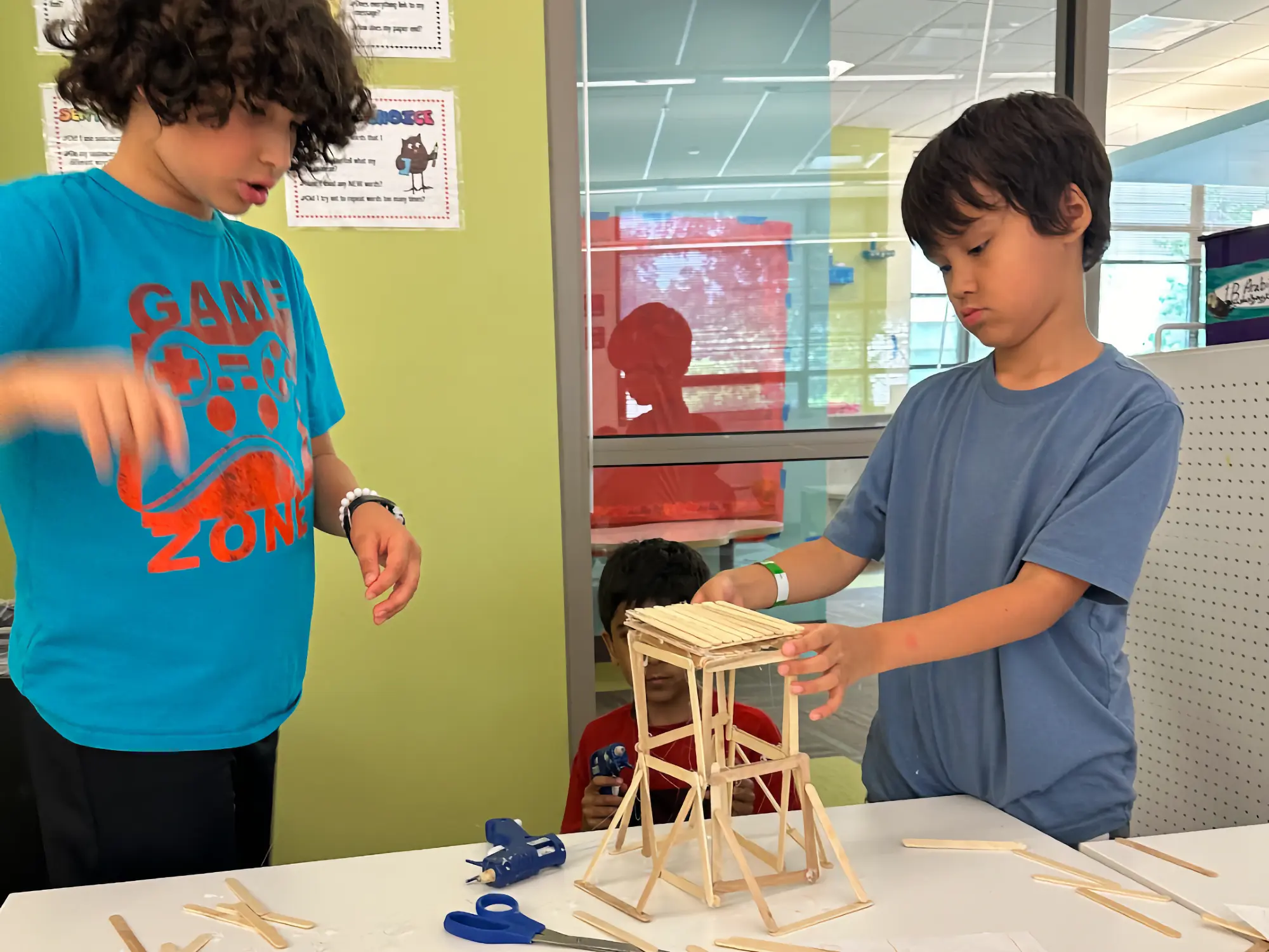 Campers building a model with popsicle sticks and a hot glue gun in a classroom.