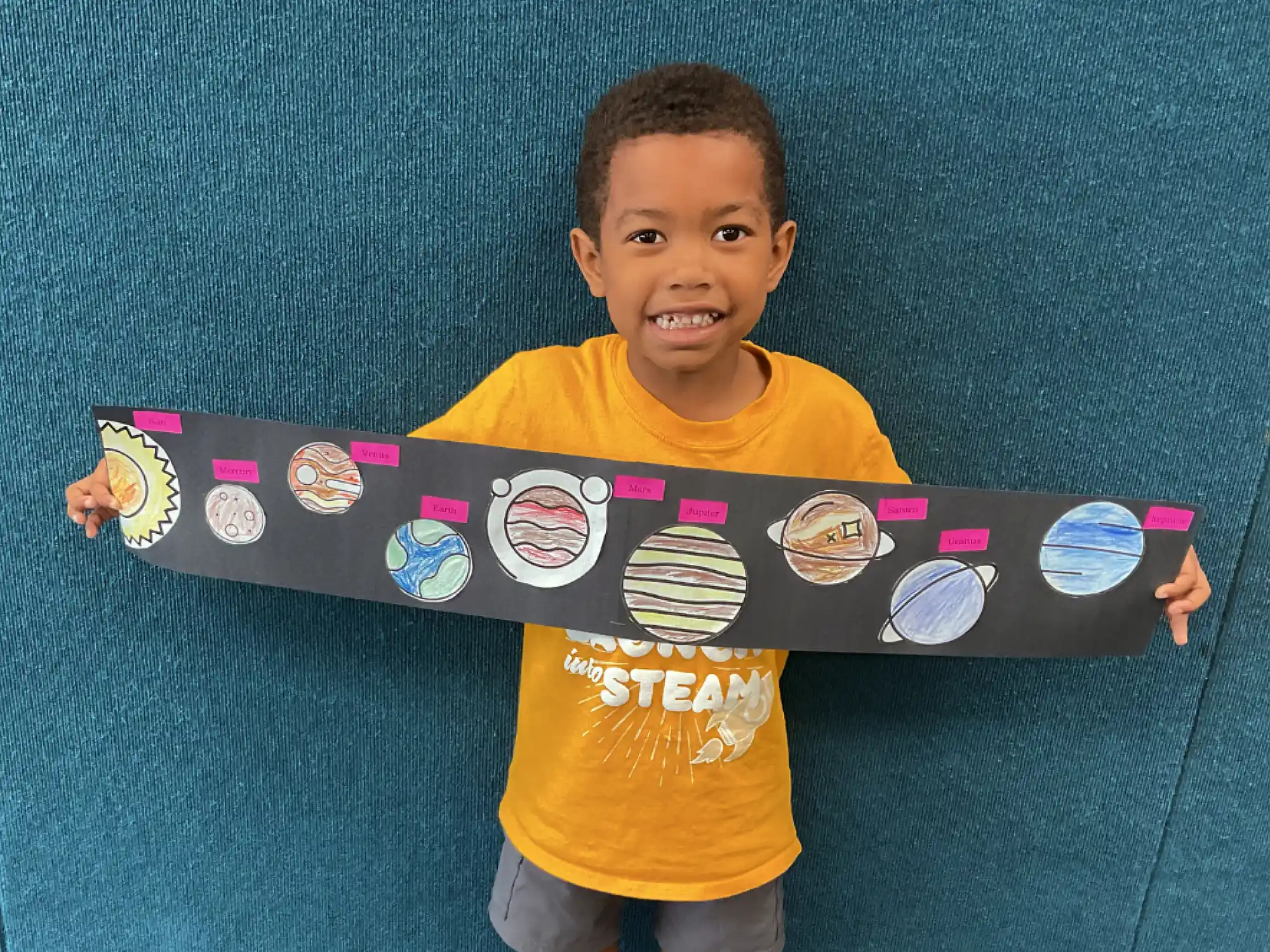 A young camper holding up a planet art project.