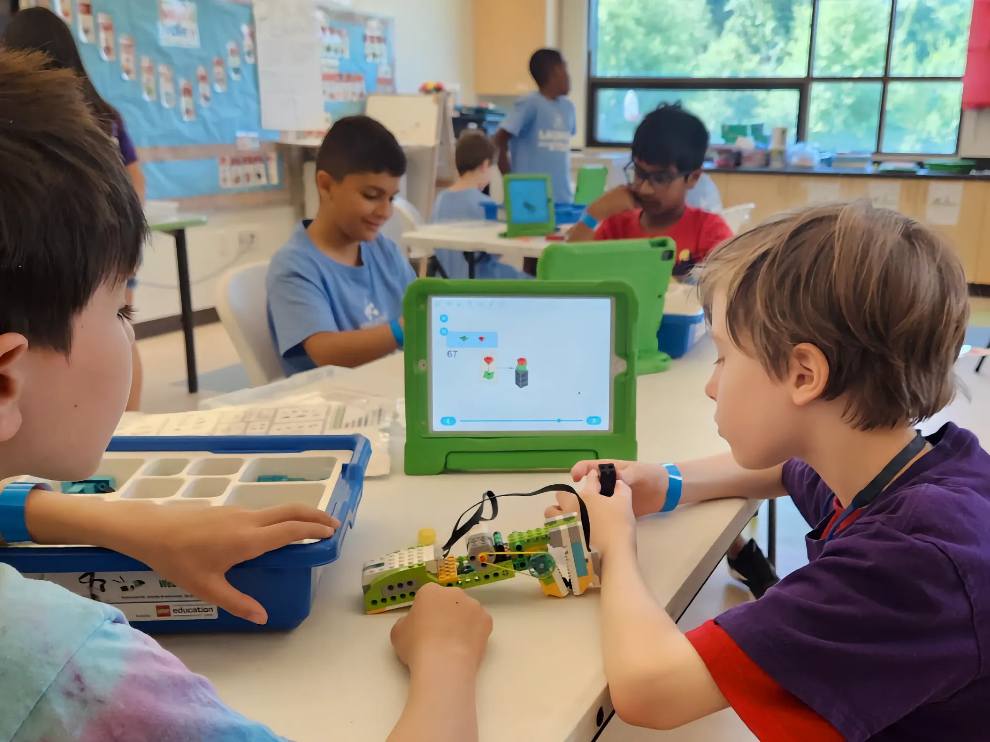 Campers working on a LEGO model along with a tablet in a classroom.